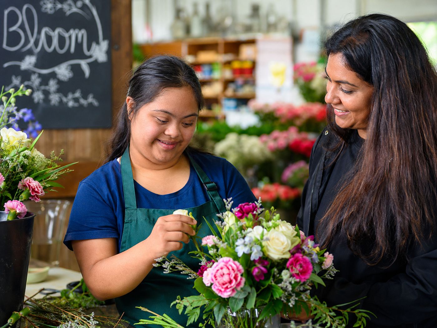 A young woman with Down syndrome arranging flowers in a florist shop alongside a colleague.